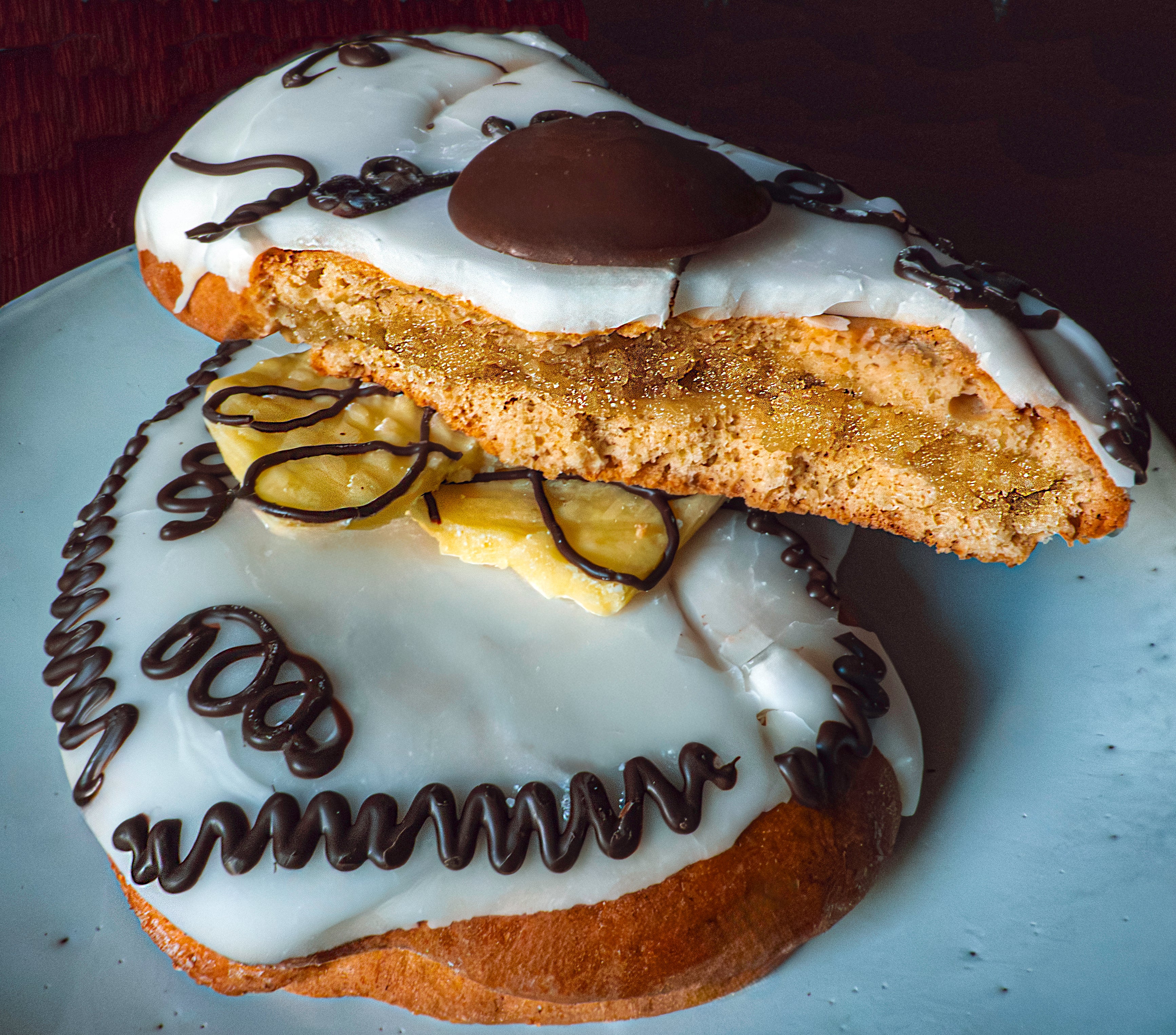 Pastry with white icing, chocolate drizzle, and a yellow filling on a white plate.