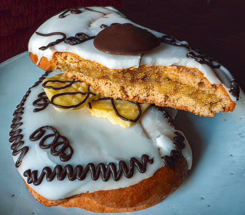 Pastry with white icing, chocolate drizzle, and a yellow filling on a white plate.